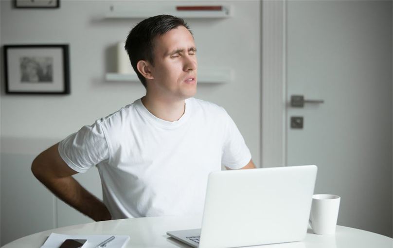 Man at a laptop holding his lower back in pain