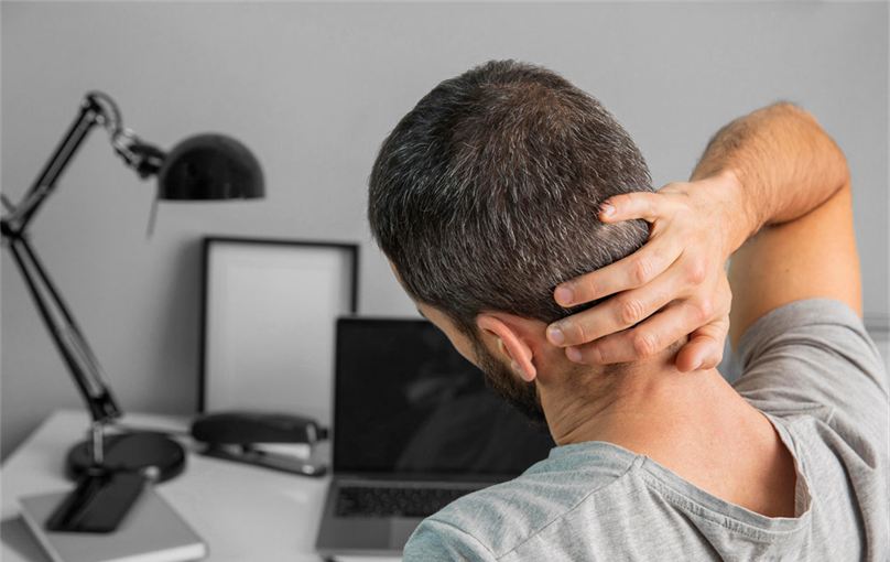 Man at his desk rubbing a tense neck